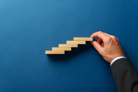 Hand of a businessman making a staircase like structure of wooden pegs in a conceptual image.